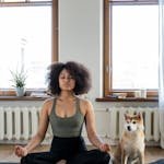 A woman practices yoga meditation at home with her dog, creating a calm and peaceful environment.